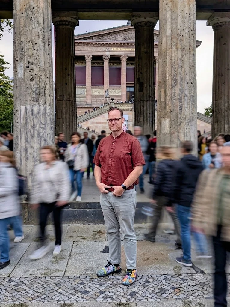Eyal in a red shirt among stone columns, with the passing crowd blurred around him
